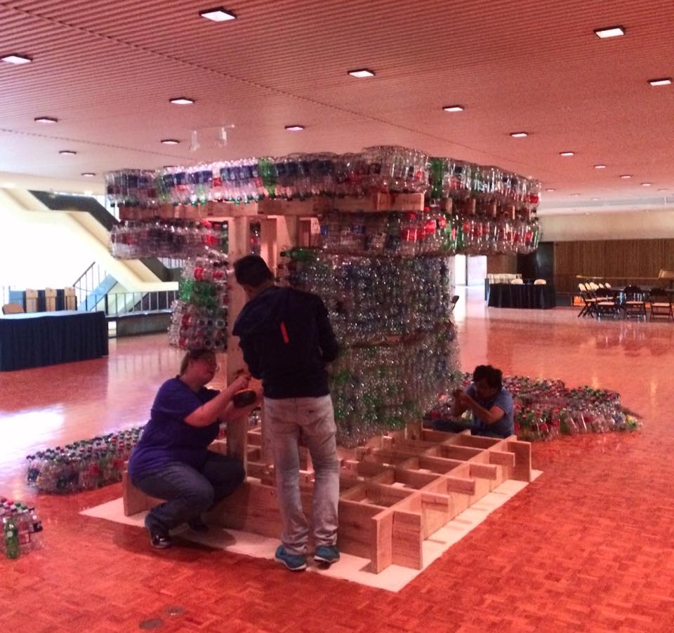 People assembling a sculpture made from beverage bottles and wood